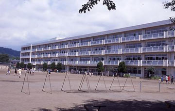 広々とした校庭の奥に建つ、白く横長の四階建ての校舎の外観写真