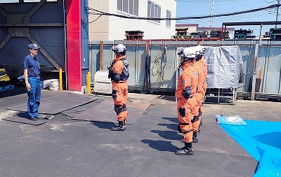 濃い青の制服を着た男性が前に立ち、向かい合わせにオレンジ色の活動服と白いヘルメットを着用した救助隊員が直立不動の姿勢をとって整列している写真