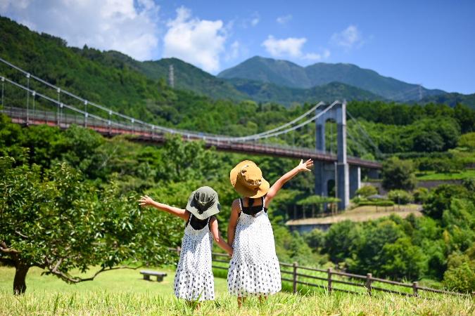 第4回秦野市インスタグラム写真動画コンテストの写真部門の優秀作品で表丹沢と県立秦野戸川公園の風の吊り橋を背景に仲良しの姉妹が手をつなぎ、元気にポーズをしている作品