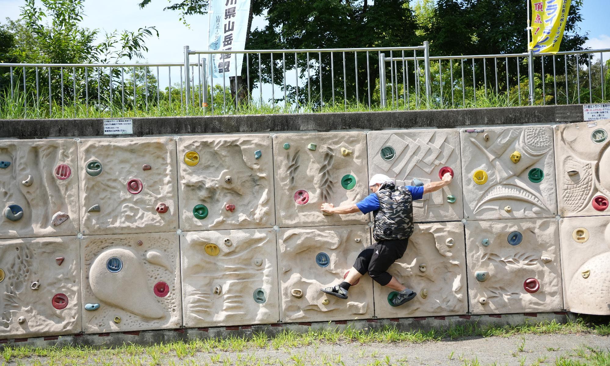 屋外の公園にある高さの低いボルダリング用の壁で、男性が壁を登っている写真