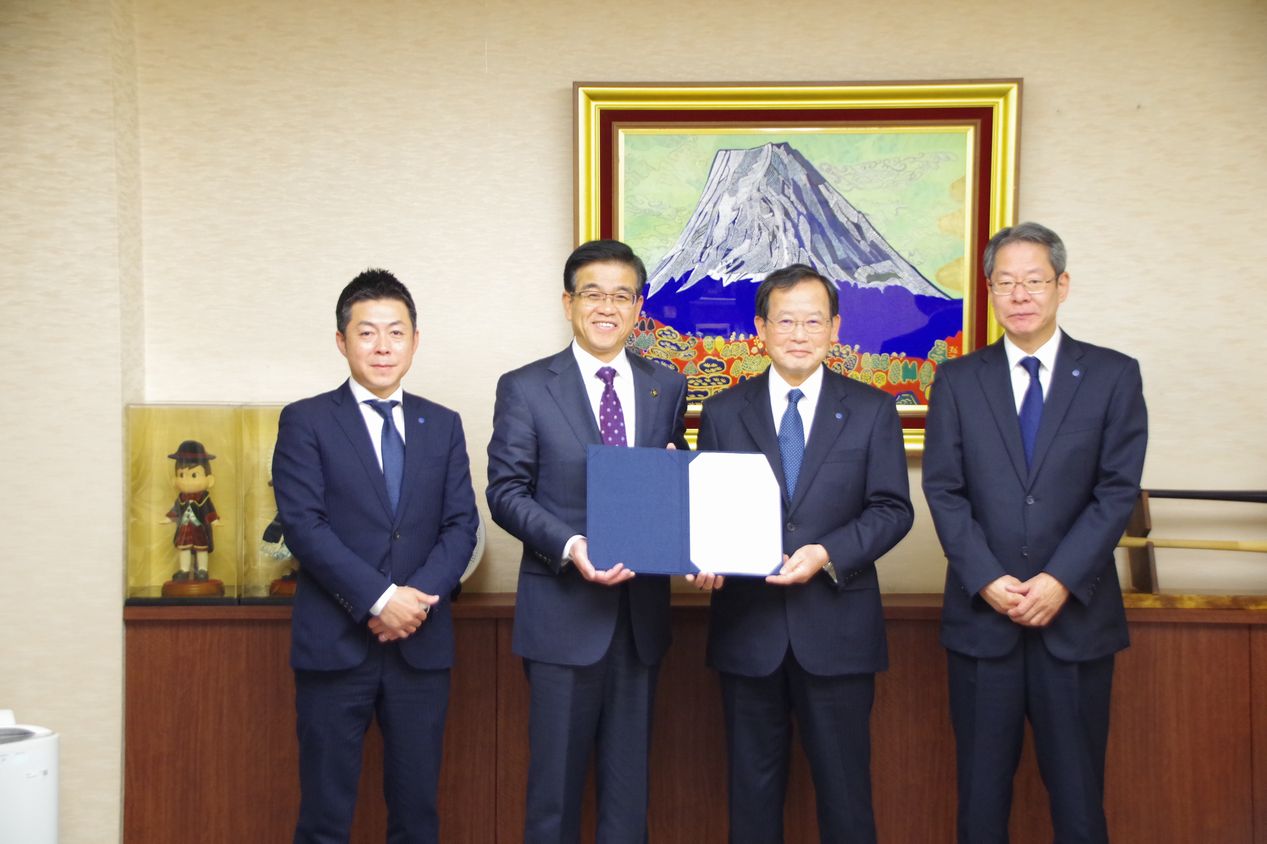 市長と中央の男性が契約書を持ちそ、その両側に1人ずつ男性が並んで立っている記念写真