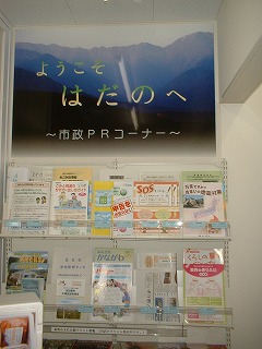 「ようこそ はだのへ 〜市政PRコーナー〜」と書かれたパネルの下に、市民向けの生活情報や防災、観光などのさまざまなパンフレットが陳列された自治体広報スペースの写真