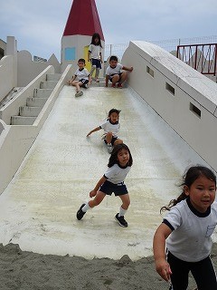 野外の大きな白いお城のような滑り台で、複数の園児たちが体操服を着用して楽しそうに遊んでいる様子を捉えた写真