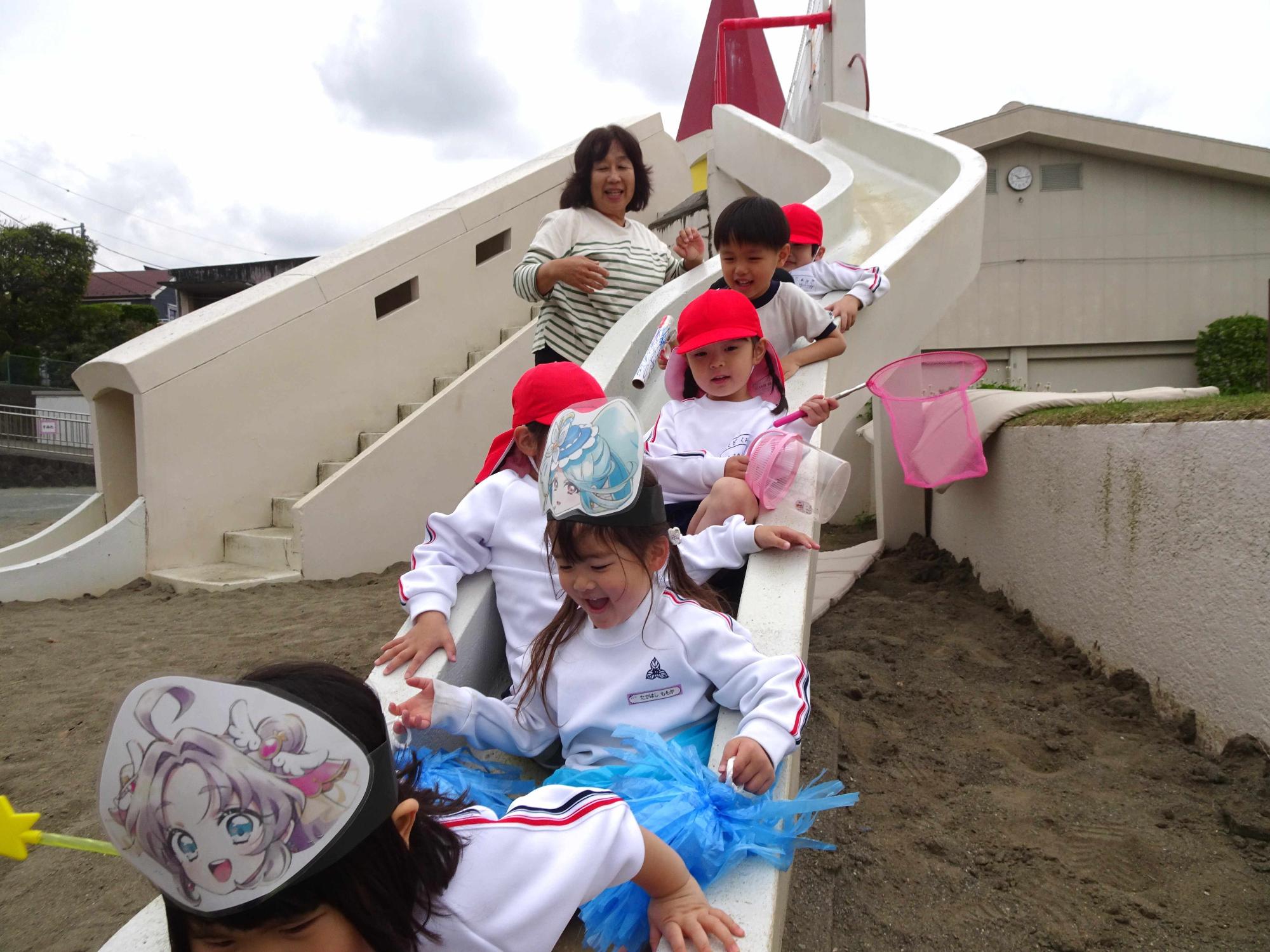年少児が園庭の大きな滑り台にみんなで登り、一斉に滑っているところです。