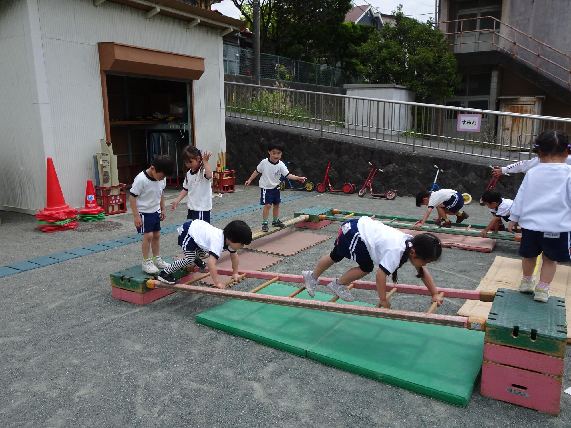 園庭に巧技台や一本橋などでサーキットを組み、年少児が挑戦しているところです。
