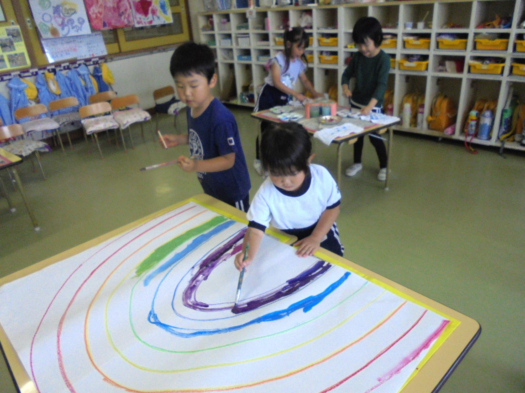 大きな模造紙に筆を使って虹を描いているところです。