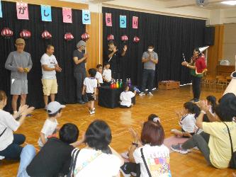 夏祭りの手品ショーで子どもと保護者が一緒に楽しんでいるところ