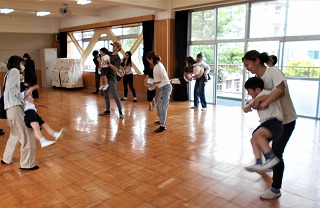 木の床の広々とした室内で、複数の保護者と園児を背中側から抱き上げ親子の触れ合いレクリエーションの様子を写した写真