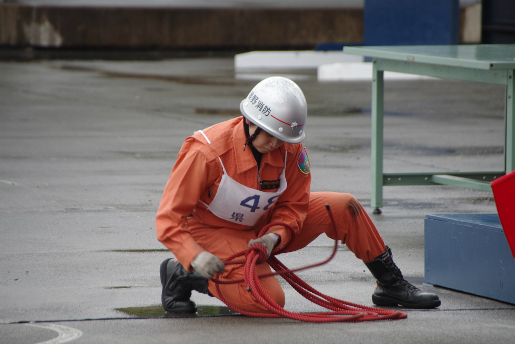 赤いロープを手にした救助隊員が、地面に片膝をつき、作業をしている様子を写した写真
