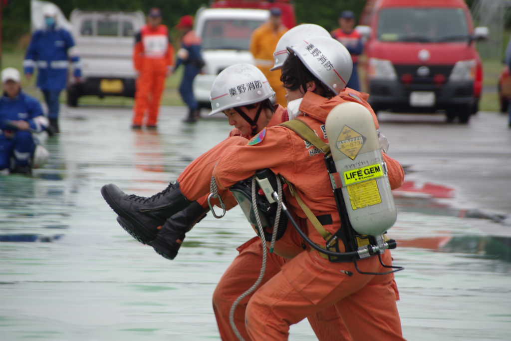 二人の女性救助隊員が、要救助者役の隊員を抱えて走っている訓練の様子を写した写真