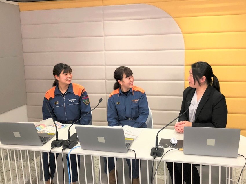 青いレスキュー服姿の女性2名とスーツ姿の女性1名が、目の前のマイクとノートパソコン越しに向き合って笑顔で話しているWebセミナーの様子の写真