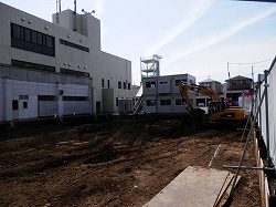 後ろには工事中の建物が見え、端には掘削機と仮設の事務所が置かれている広大な空き地の写真