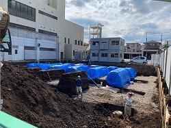 建物の工事の基礎部分で、掘り起こされた土が山積みになっており、その一部が青いビニールシートで覆われている写真