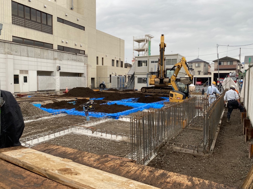 重機や鉄筋、土嚢が置かれコンクリートが流し込まれた基礎工事の現場で、ヘルメットを被った複数の作業員が作業をしている写真