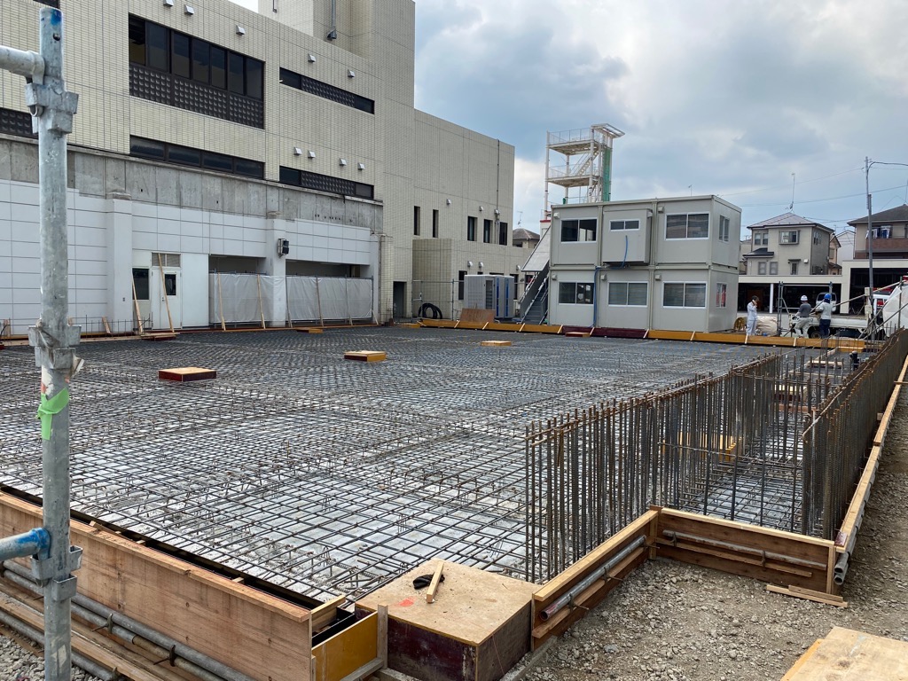 鉄筋が格子状に組まれ、その周りを木の型枠が囲んでいる、基礎工事中の建物の写真