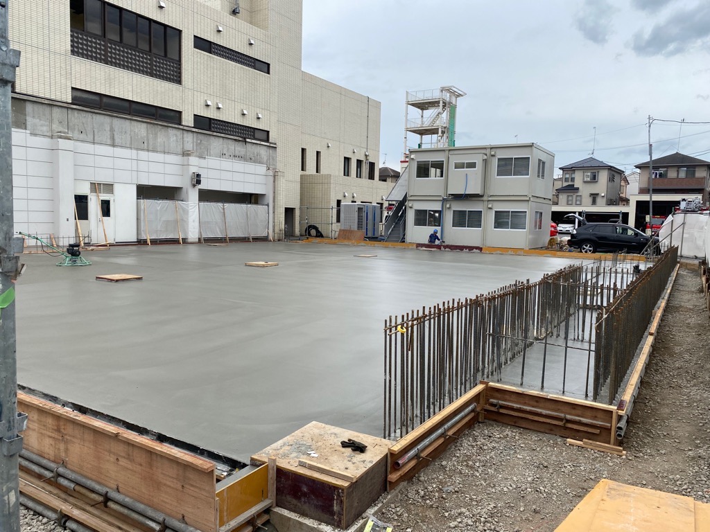 建物の基礎工事の様子で、鉄筋の骨組みが組まれ、コンクリートが流し込まれた広大な地面が平らになっている写真