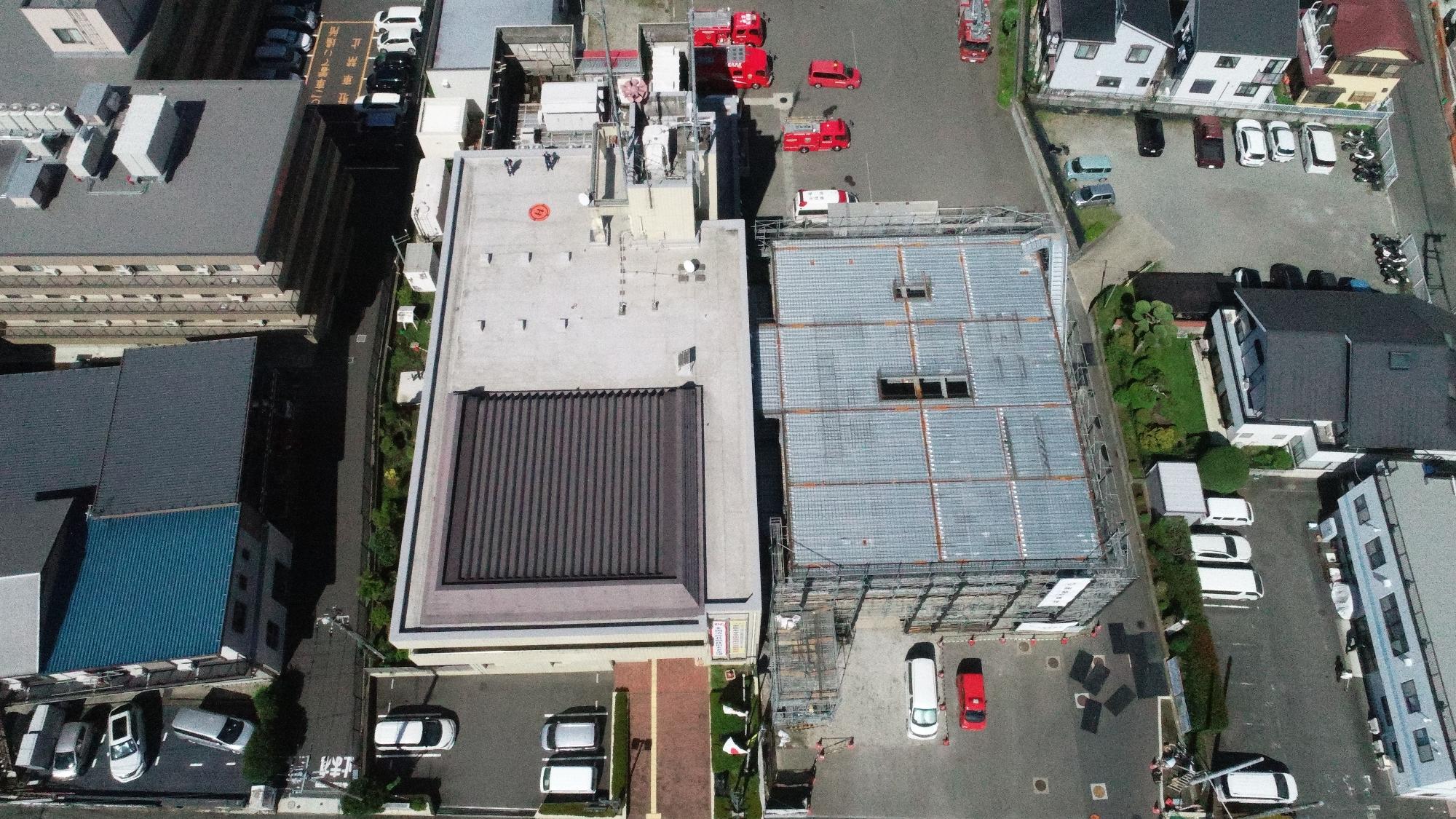 一方には足場が組まれ、もう一方には空調機が並んでいる屋上の工事現場の様子をドローンで写した写真