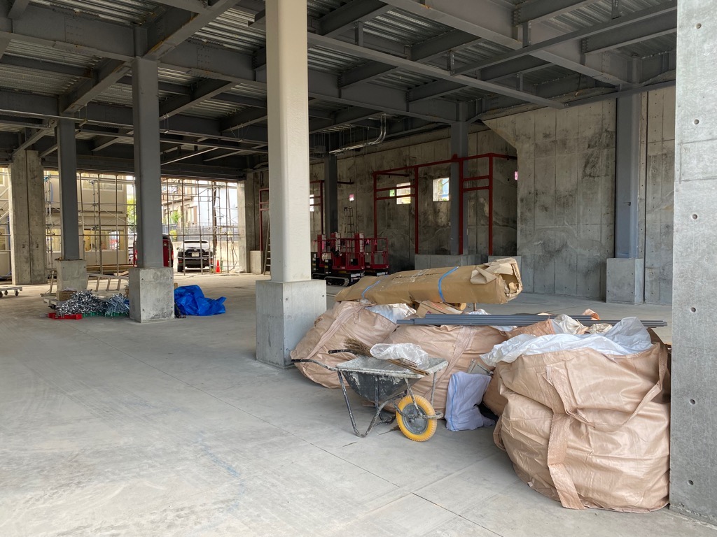 床に大きな土嚢袋が山積みになっており、天井や壁の骨組みがむき出しになっている建設中の建物の写真