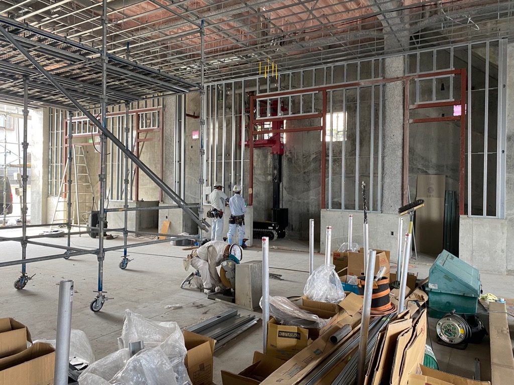 骨組みがむき出しになった建設中の建物の屋内で、ヘルメットを被った複数の作業員が作業をしている写真