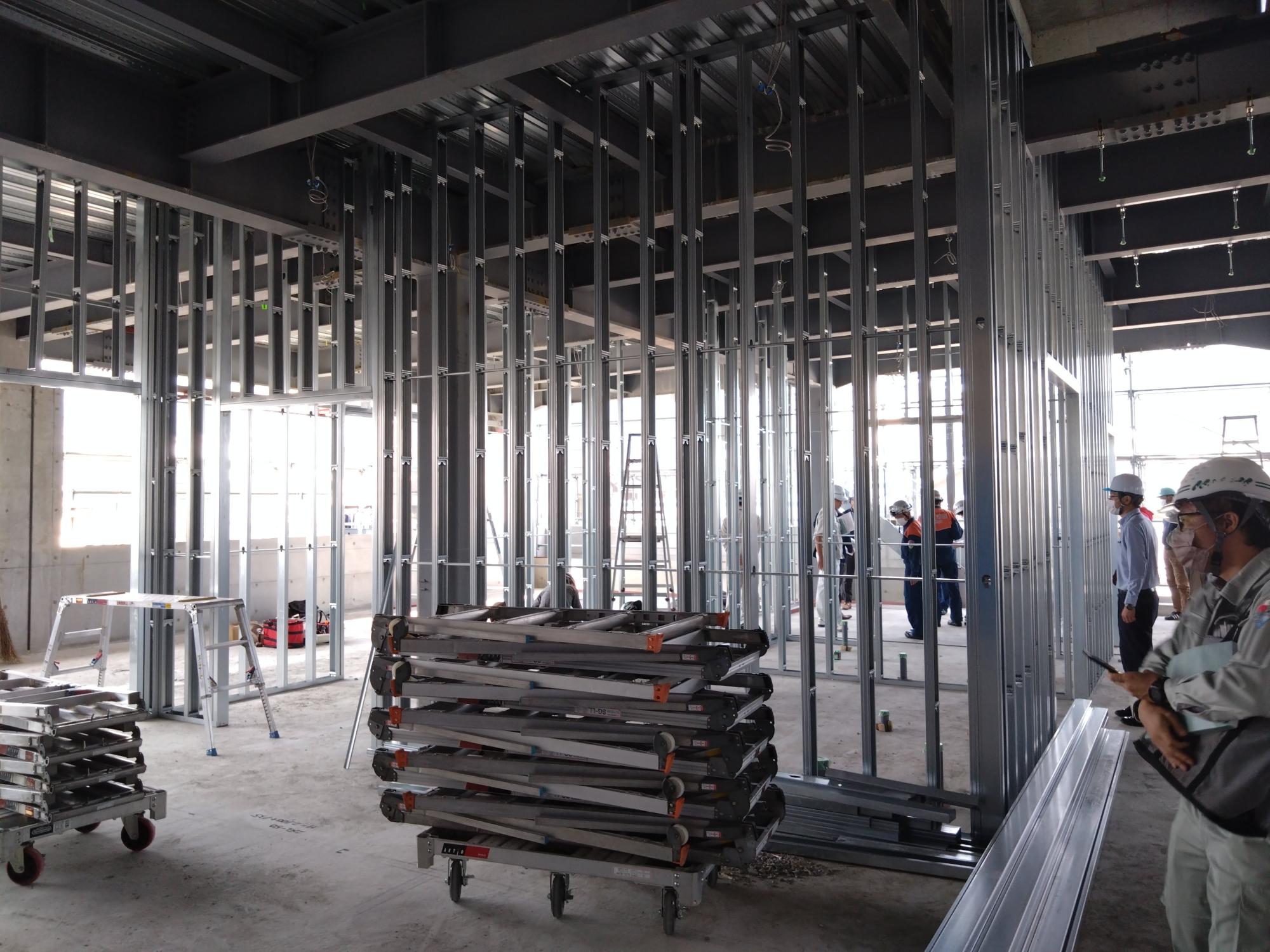 金属製の柱と梁で骨組みが組み立てられた、建設中の建物で、複数の作業員が作業をしている写真