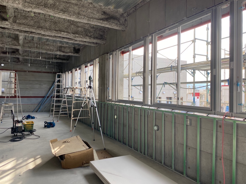 複数の梯子と脚立が立てかけられており、足場が組まれた窓の外からは建設中の建物の様子が見える写真