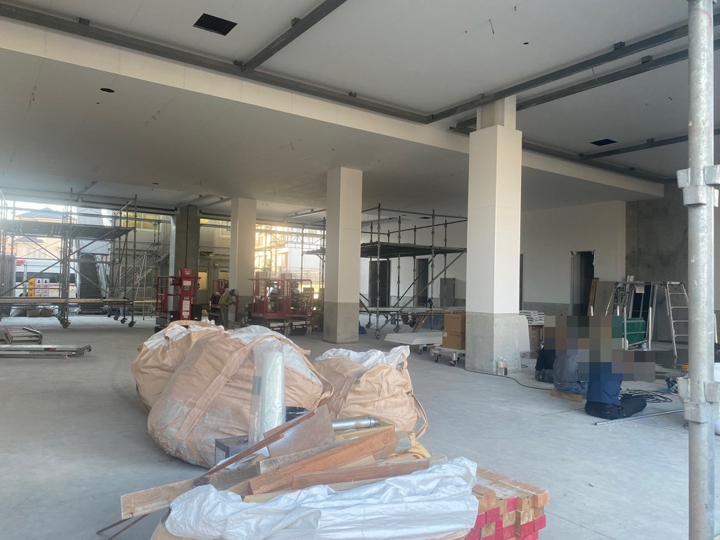 鉄骨の足場が組まれ、柱や梁がむき出しになった建設中の建物の屋内で、資材が山積みになり、複数の作業員が作業をしている車庫内の写真