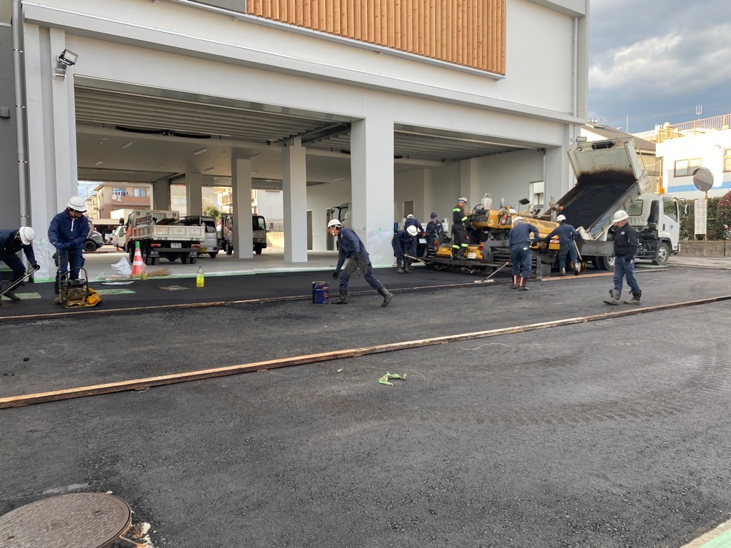 建設現場で複数の作業員が、アスファルトの舗装作業をしている様子を写した写真