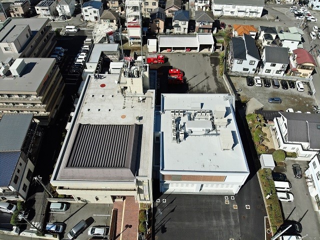 建物の屋上や駐車場が広角で写っており、周りを住宅街に囲まれている消防署の建物の空撮写真