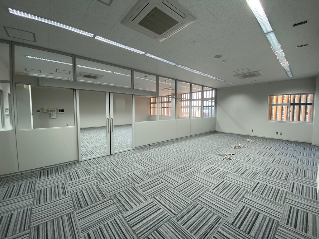 複数の白いパーティションとガラス張りの扉で仕切られた、床に幾何学模様のカーペットが敷かれている指令室の写真