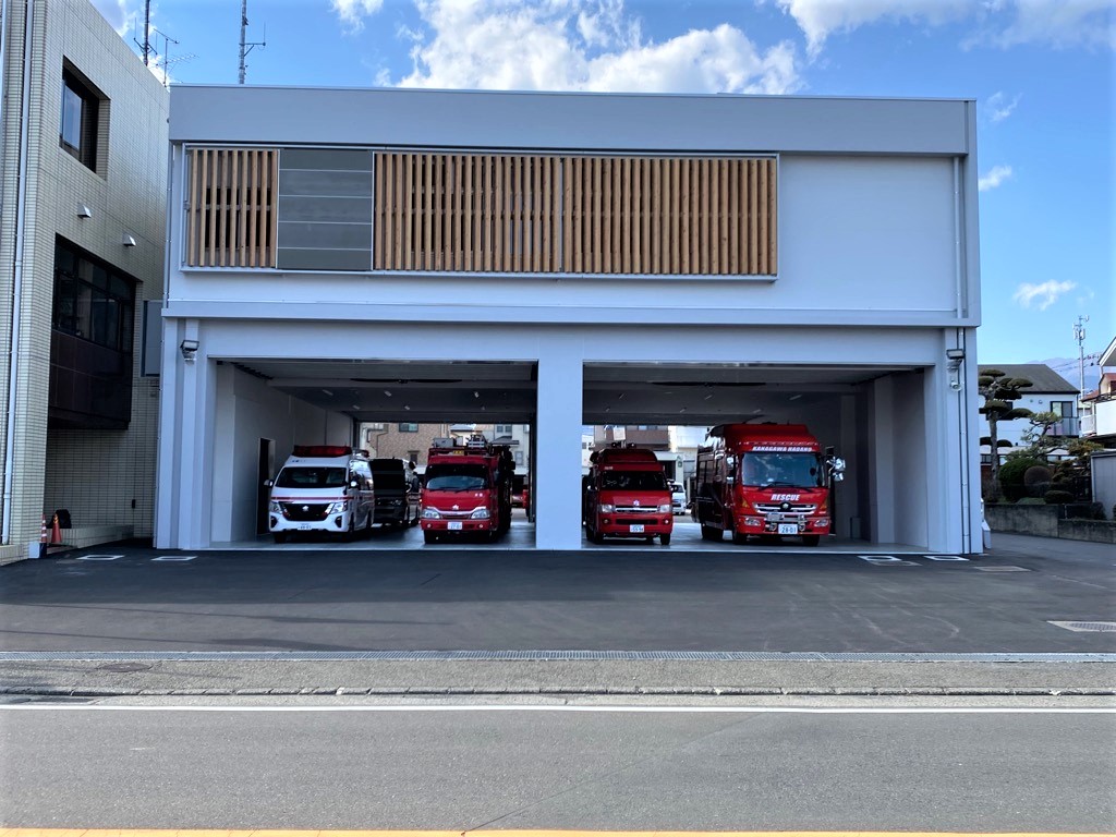 白い近代的な建物にある車庫に、赤い消防車や救急車が複数並んでいる消防署を正面から写した写真