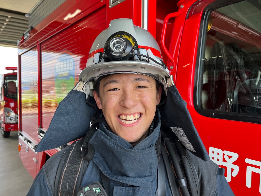 防火服を着用し、あご紐を外した銀色のヘルメットをかぶった白石 純也さんの写真