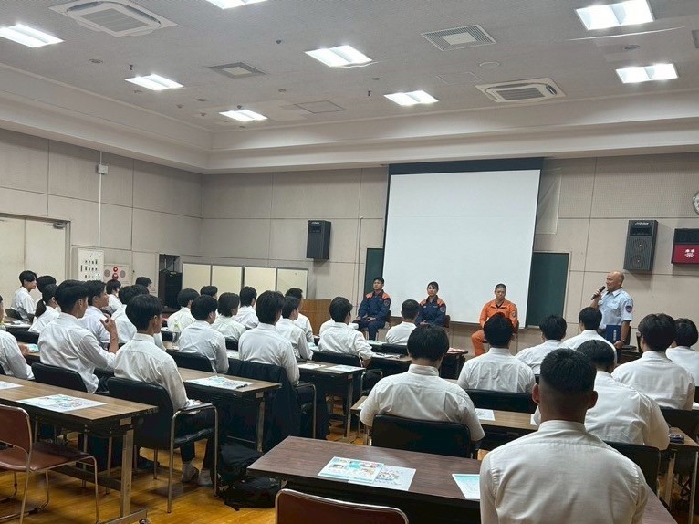 職員がスライドを投影しながら、多数の生徒または職員に向かって講義している様子を写した写真