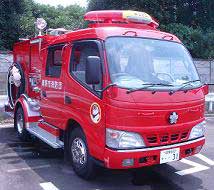 明るい赤色に塗装され、ルーフに黄色い警光灯とサイレンスピーカー、側面にホース格納部を備えた、一般的な中型の消防ポンプ自動車の写真