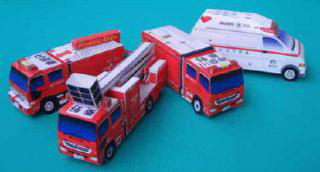 青緑色の背景に、はしご車を含む3台の赤い消防車と1台の白い救急車、合計4台の緊急車両のペーパークラフトが並べられている写真