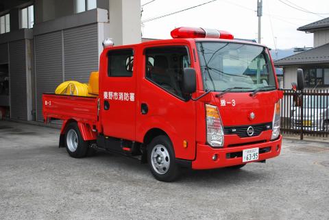 赤色の小型トラック型の消防車で「秦野市消防署」と書かれ、荷台に黄色いホースが積まれている消防署西分署の消災害対応搬送車が車庫の前に停車している写真