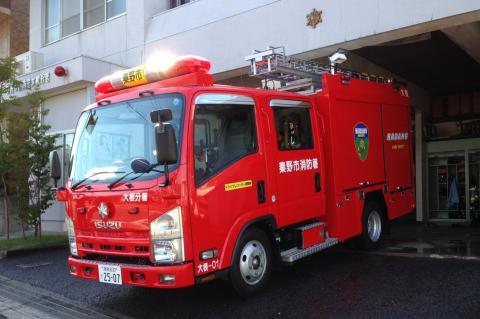 真っ赤な車体の中型消防車が消防署の前に停められ、車体には「秦野市消防署」と白文字で書かれていて、屋根には赤色灯とハシゴが積まれている消防署大根分署の消防ポンプ自動車の写真