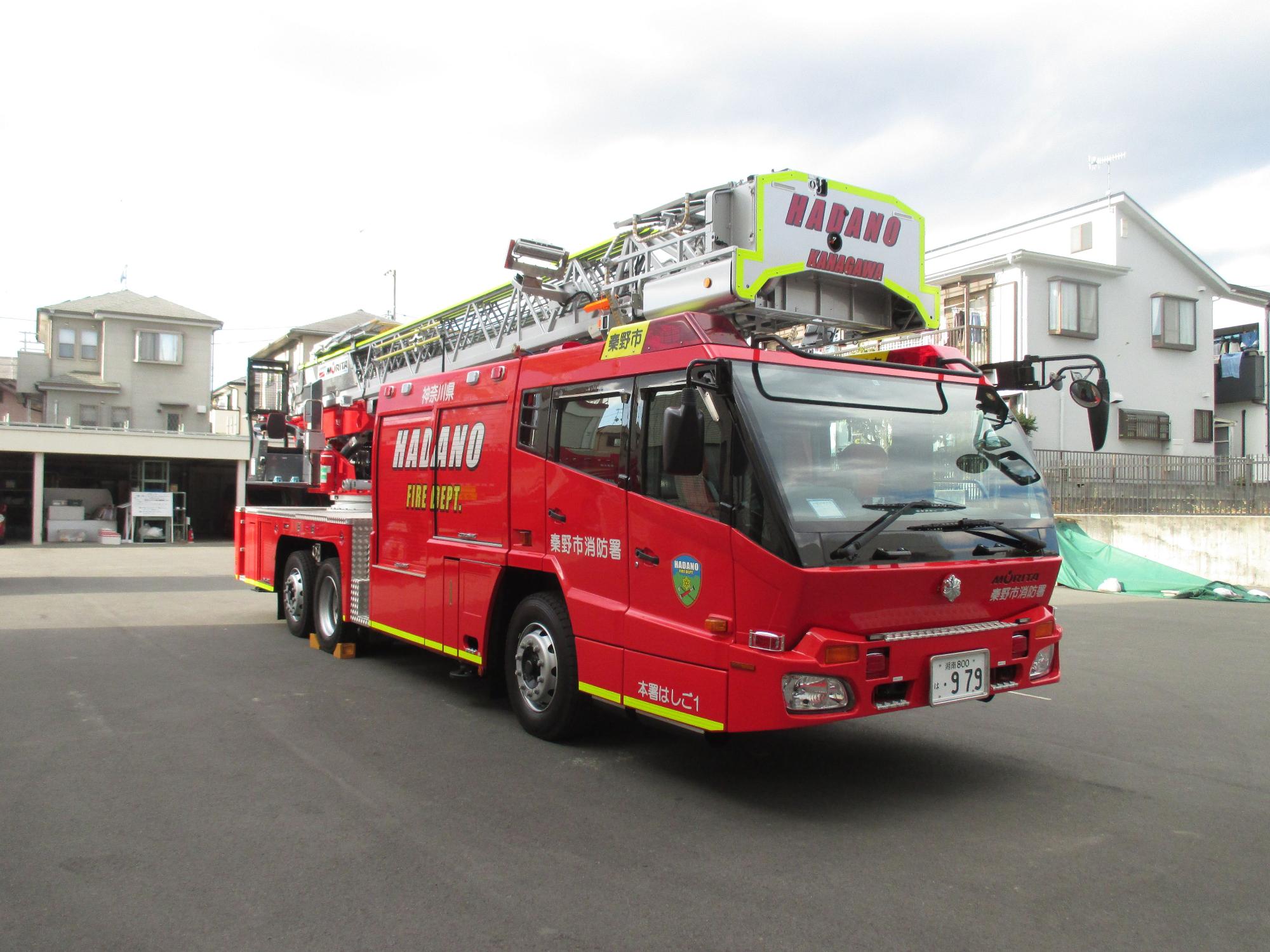 大型のはしご付き消防車で、上部の長いはしごに「HADANO」と書かれており、災害現場で高所作業ができる消防署本署のはしご車の写真