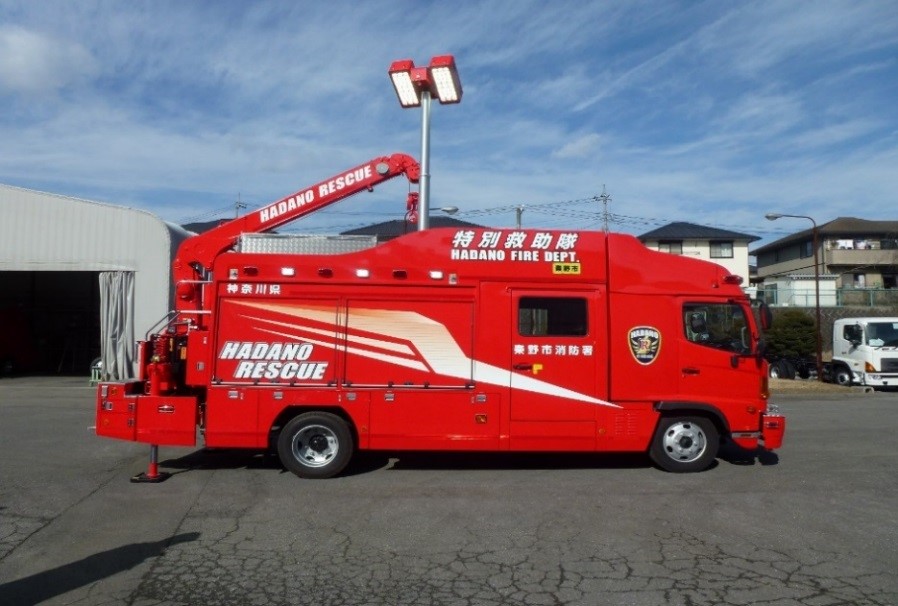 赤い車体に「HADANO RESCUE」と書かれた救助工作車で、車体後部には小型クレーンのようなアームがあり、消防署本署の工作車を横から捉えた写真