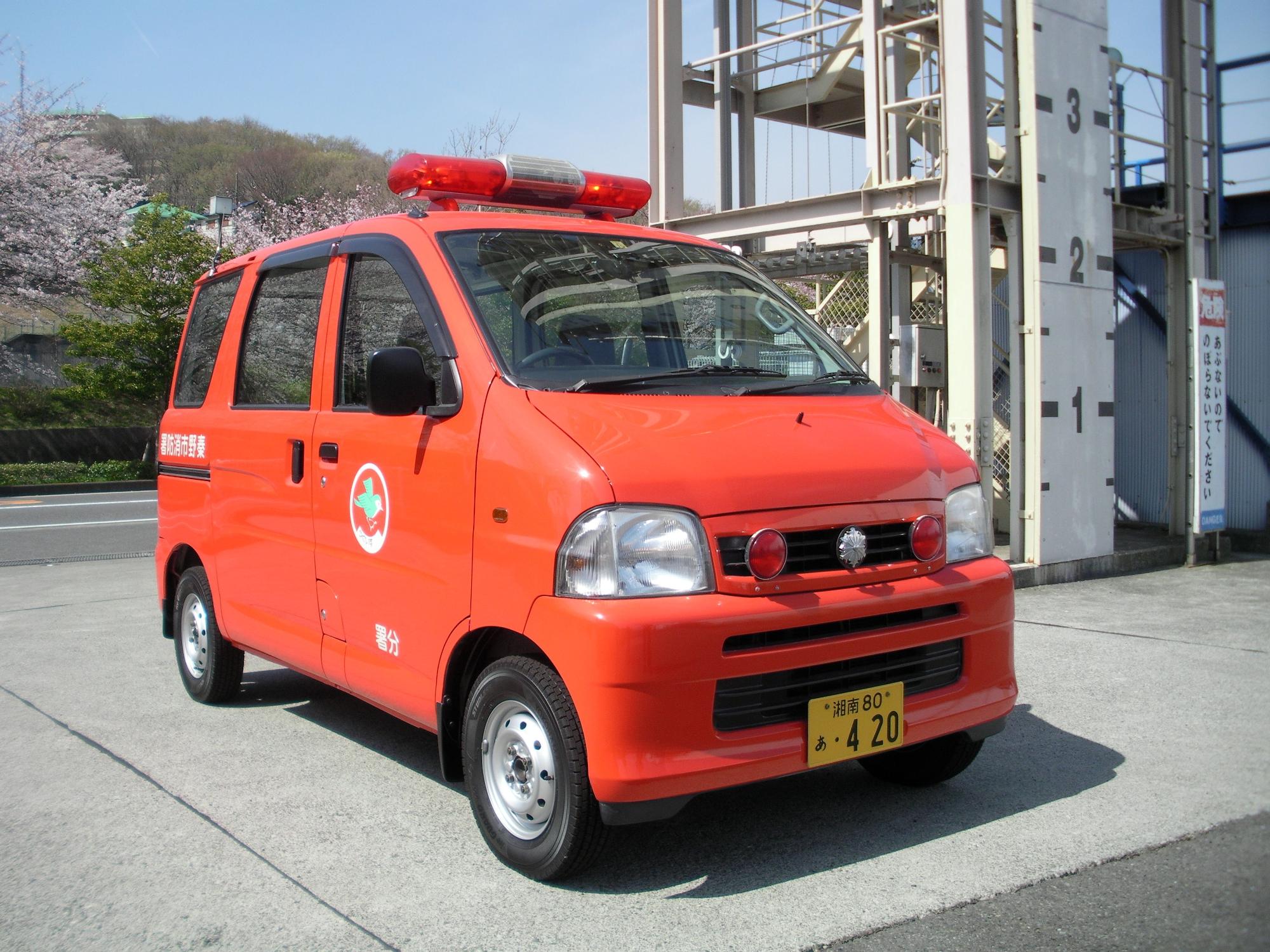 赤色の軽ワゴン車で、屋根に赤色灯を備えた消防署本署の小型搬送車が、屋外に停まっている写真