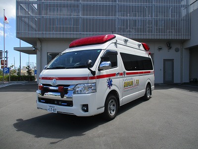 白地に赤いラインが入った救急車が建物の前に停車しており、車体には「KANAGAWA HADANO F.D.」と書かれ、横に青い救急マークがある消防署西分署の救急車の写真