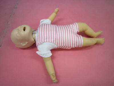 ピンク色のジョイントマットの上に、ボーダーの服を着た救命講習用の乳児のマネキンが、仰向けに置かれている心肺蘇生訓練人形（乳児ピンク縞）