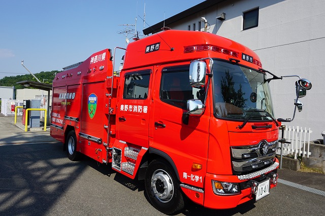 赤色の車体に「神奈川県」「秦野市消防署」と書かれ、赤色灯や機材を搭載した消防署南分署の化学車が、建物の横に駐車している写真
