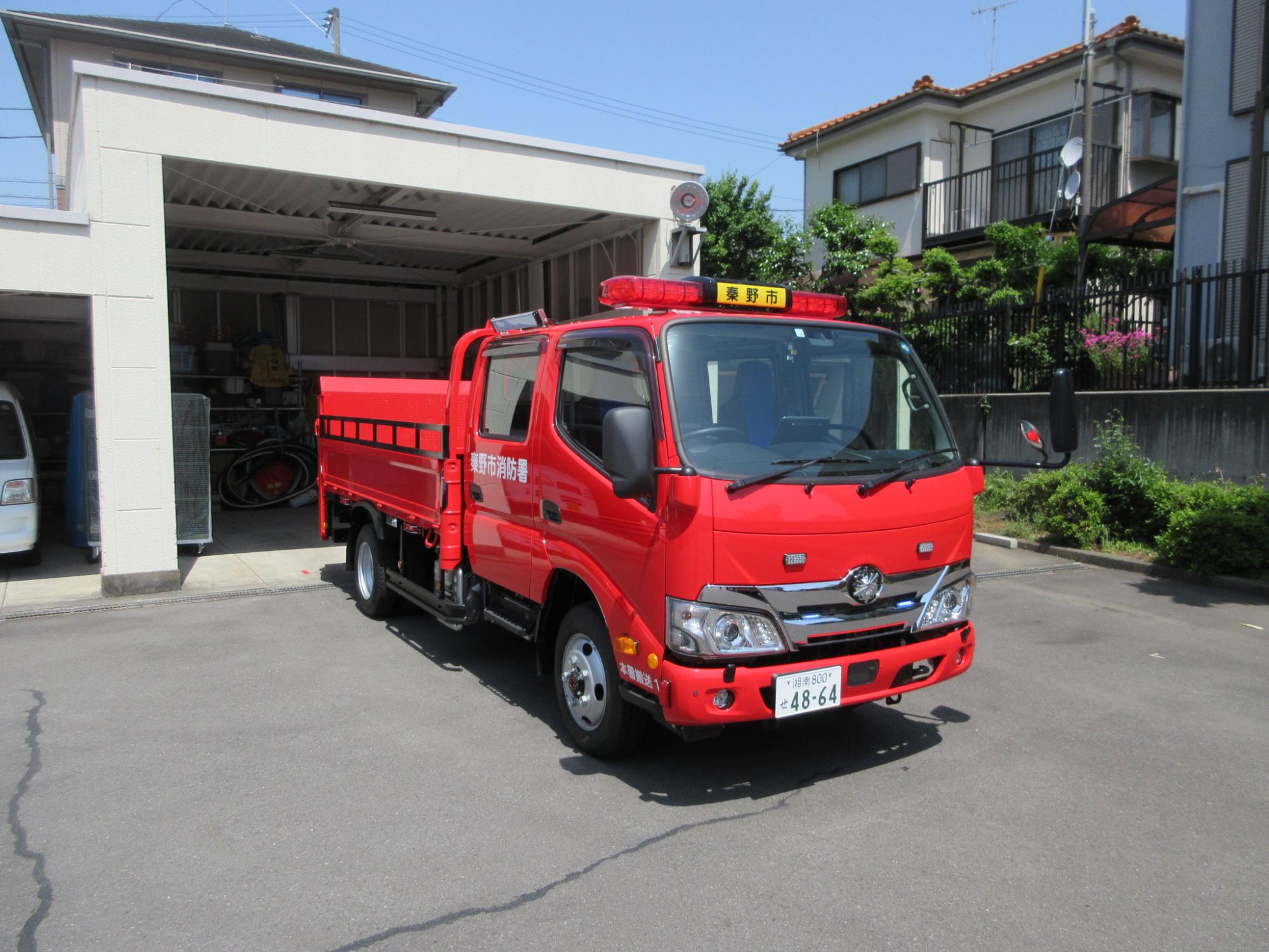 赤色の小型トラックで、荷台が柵で囲まれており、上部には赤色灯とスピーカーが搭載されている消防署本署の資機材搬送車の写真