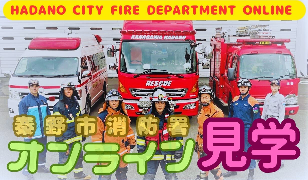 鮮やかな赤い消防車、レスキュー車、救急車が並んだ格納庫の前で、防火服や活動服姿の七人の消防職員が正面を向き、手前に「秦野市消防署 オンライン 見学」と重ねて表示されている、秦野市消防署のオンライン見学案内画像の写真