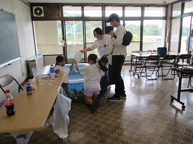 集会所らしき室内で、ビニールプールを囲んで複数の親子が集まり、イベントに参加している様子の写真