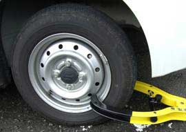 停車している自動車のタイヤホイールに黄色と黒の配色のタイヤロックが装着されている写真