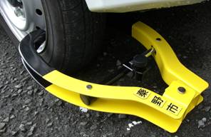 タイヤホイールに装着されている、黄色と黒の配色で、「秦野市」の文字が書かれたシールが貼られたタイヤロックのアップ写真