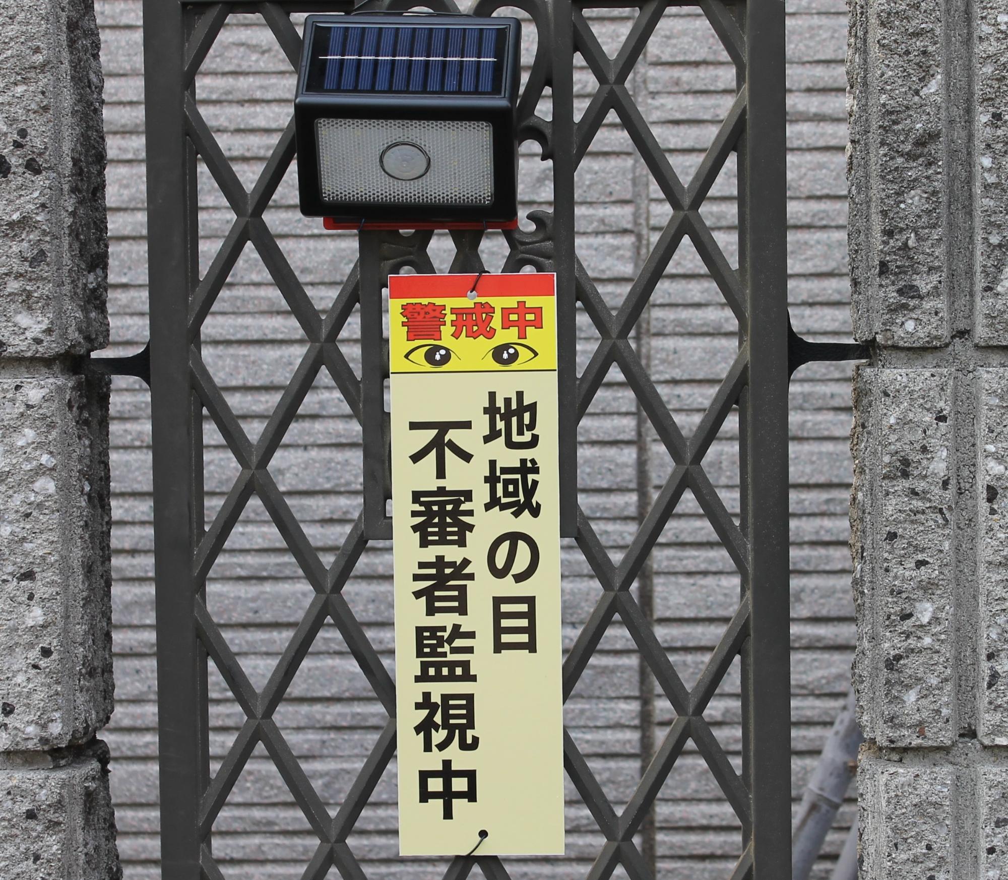 防犯センサーの下に「地域の目 不審者監視中」と防犯プレートがせ設置されている様子を写した写真