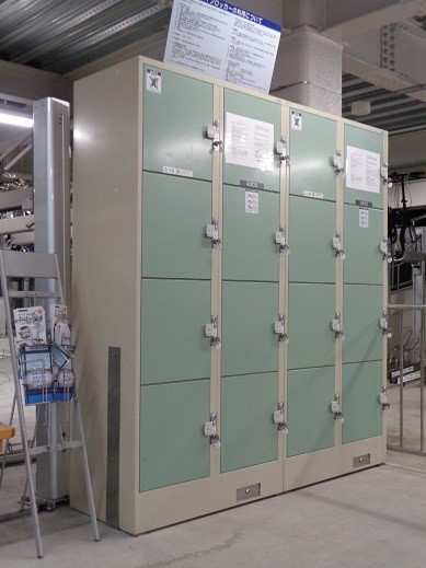 上部に利用に関する注意事項が書かれた掲示物が貼付されている、薄い緑色の扉の四列四段のコインロッカーの写真
