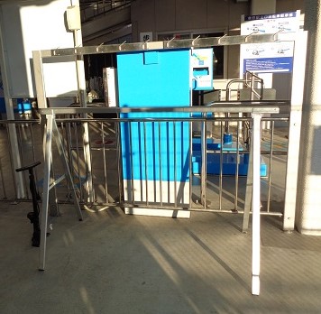 手前のステンレス製のフェンスの後ろにシルバーの自転車ラックと利用案内の看板がある様子の写真